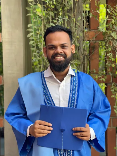 Niaz Nafi Rahman in a graduation gown, holding a mortarboard.